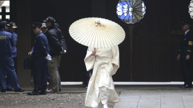 A shrine worker puts up an umbrella as he walks past the police officers after an explosion was reported at the shrine's restroom.