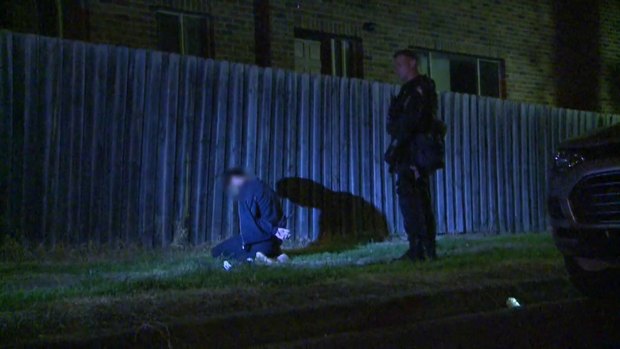 One man detained by police kneels on the ground as a raid is carried out. 