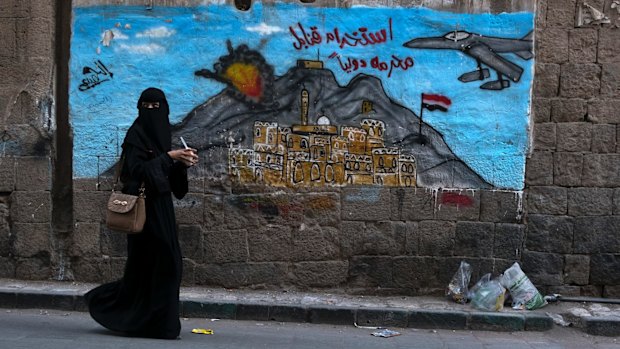 A woman passes a mural depicting airstrikes in Sanaa, Yemen.