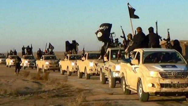 An undated file photo released by a militant website shows militants of the Islamic State group holding up their weapons and wave flags on their vehicles in a convoy on a road leading to Iraq, while riding in Raqqa, Syria. 