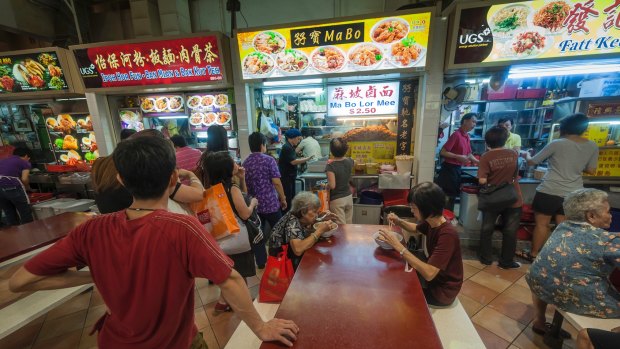 Local people queue at street food stalls in a hawker food market in downtown Singapore.