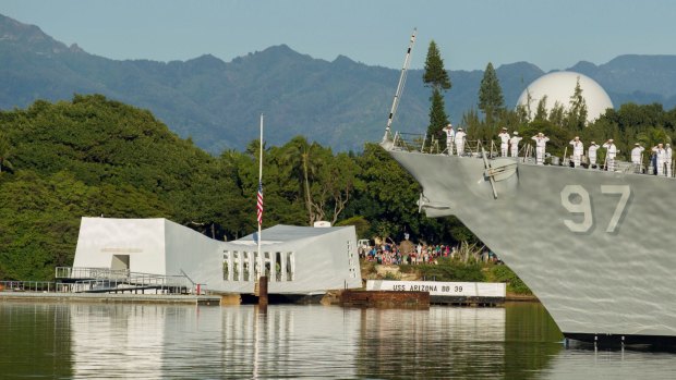 Sailors on the USS Halsey salute while passing by the USS Arizona Memorial.