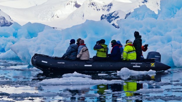 Tourists explore rugged blue icebergs cruising in an inflatable boat. 
