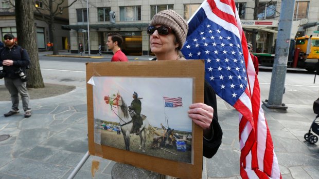 Dianne Reeves, of Seattle, holds an upside-down U.S. flag, commonly seen as a sign of distress, and a photo from the Standing Rock oil pipeline protests, in Seattle.