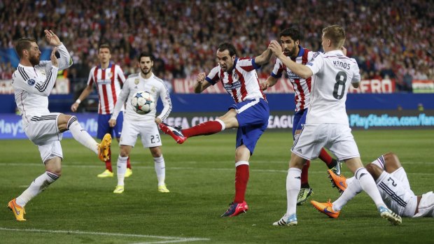 Atletico's Diego Godin, center, shoots past Real Madrid's players.