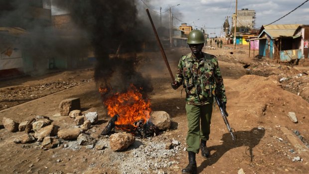 A riot policeman walks past burning barricades erected by protesters throwing rocks, during clashes in the Kawangware slum of Nairobi, Kenya.
