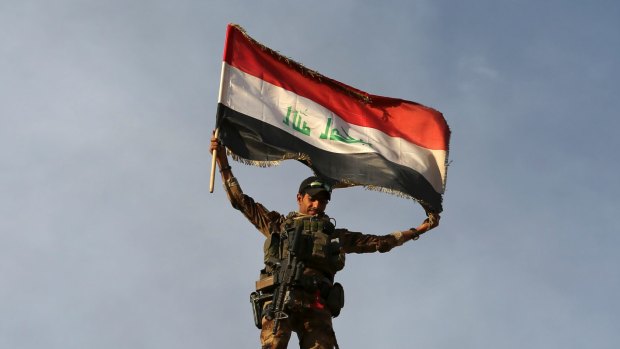 A member Iraq's elite counterterrorism forces raises an Iraqi flag after retaking Bartella, outside Mosul.