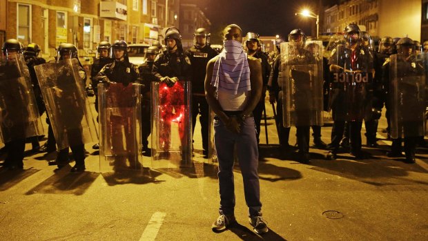 A man stands in front of a line of police officers in riot gear as part of a community effort to disperse the crowd ahead of a curfew in the wake of riots following the funeral for Freddie Gray.