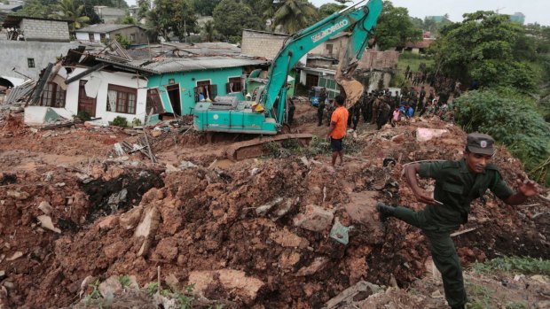 Sri Lankan army soldiers and rescue workers stand near buried houses.