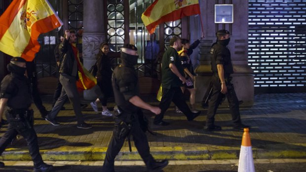 People hold Spanish national flags while being escorted by Mossos d'Esquadra, the Catalan police force.