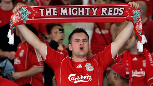 A Liverpool football fan holds up a scarf in the stands during a match.