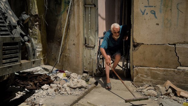 Abdulsalam Abdulqadir, 73, sweeps outside his gate from his wheelchair at the entrance of his home in West Mosul, Iraq.