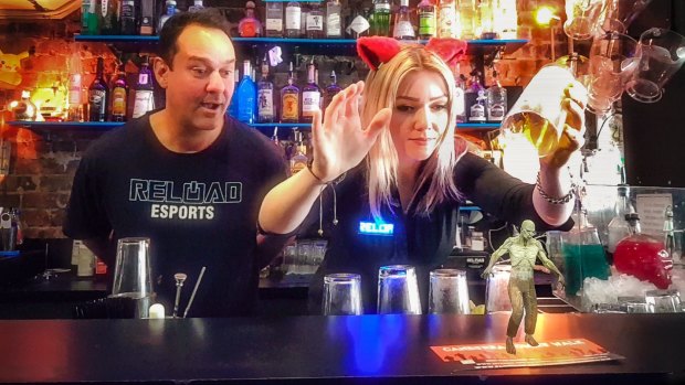 Reload Bar co-owner Ravi Sharma watches manager Hollie Lehmann attempt to catch a zombie with a beer glass in Australia's first augmented reality bar. The scene is photographed on a phone using the bar's app.