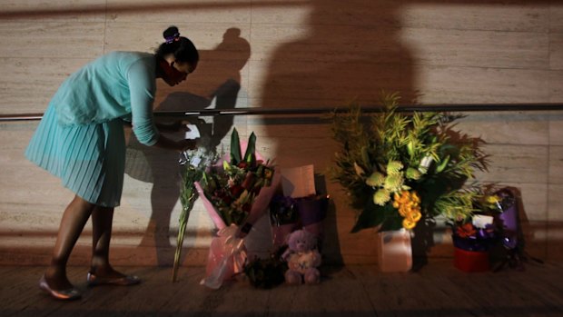 A young girl leaves flowers at the front of NSW Police Headquarters in memory of police employee Curtis Cheng.