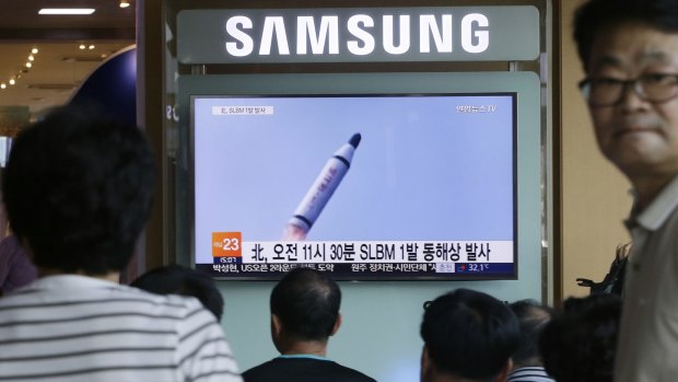People watch a TV news program showing a file footage of North Korea's submarine-based ballistic missile.