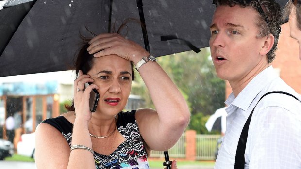 Queensland Premier Annastacia Palaszczuk is shielded from the rain by her media advisor as she takes a phone call.