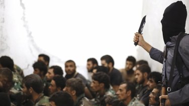 An IS militant stands over captured Syrian army soldiers and officers in August last year.