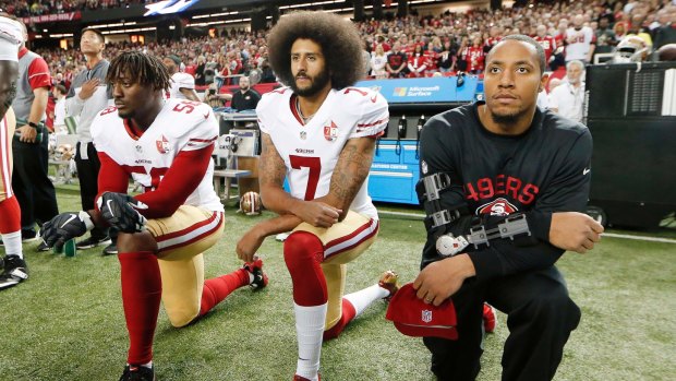 Former San Francisco 49ers quarterback Colin Kaepernick (centre) kneels during the US national anthem.
