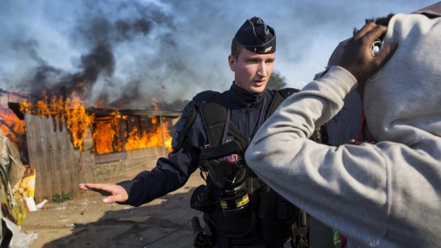 A police officer stands guard as migrant shelters burn down in the Jungle on Tuesday.