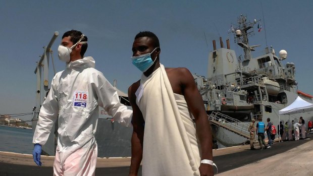An Italian paramedic helps a migrant as 402 migrants disembark from the Britain Royal Navy's ship Echo in the harbour of Brindisi, Italy, in June.