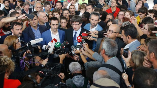Catalan President Carles Puigdemont, centre, speaks to the media at a sports center, assigned to be a polling station.
