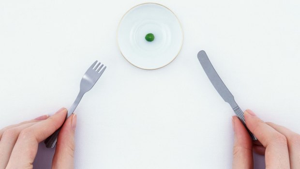 Woman holding miniature knife and fork by plate with single pea tiny plates. Serving size.