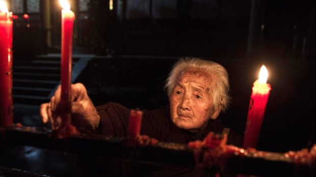 An elderly Chinese resident lights candles before morning prayers at the Ji Xiang Temple and nursing home in Sha County, Fujian province, China. 