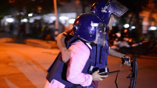 Bangladeshi police take cover near a restaurant that has been attacked by unidentified gunmen.