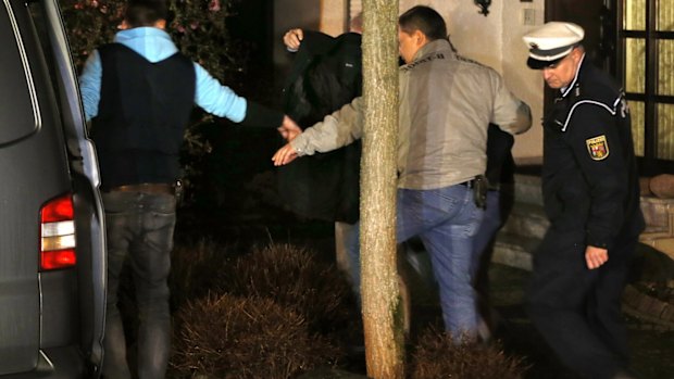 A person covered with a black blanket is led by police officers from the Lubitz family house in Montabaur on Thursday.