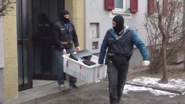 Masked police officers carry computers out of a house in Graz, Austria. 