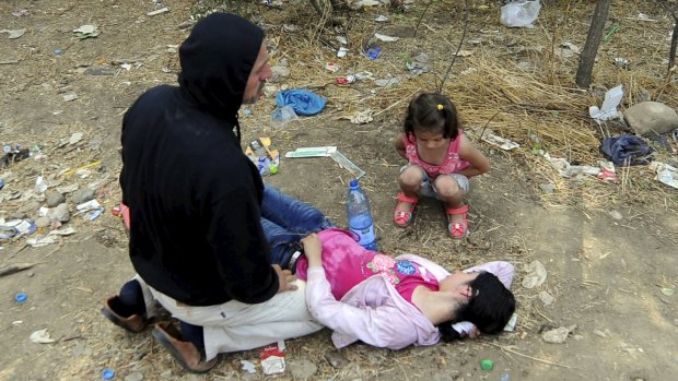 A man kneels next to his collapsed wife at the border.