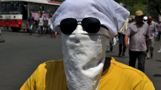 An Indian man covers his face as drives on a scooter under the hot sun in Hyderabad.