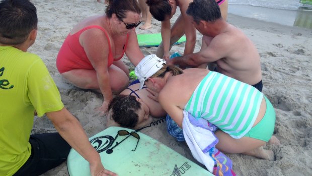 People assist a teenage girl at the scene of a shark attack in Oak Island