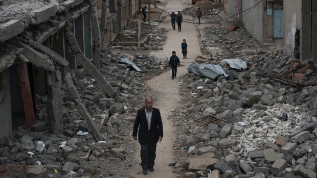 Iraqi civilians walk in a neighborhood recently liberated by Iraqi security forces on the western side of Mosul, Iraq.