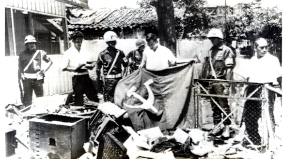 Indonesian police hold a communist flag in the ruins of Indonesian Communist Party  House in Jakarta after it was ransacked by anti-communist demonstrators in 1965.  