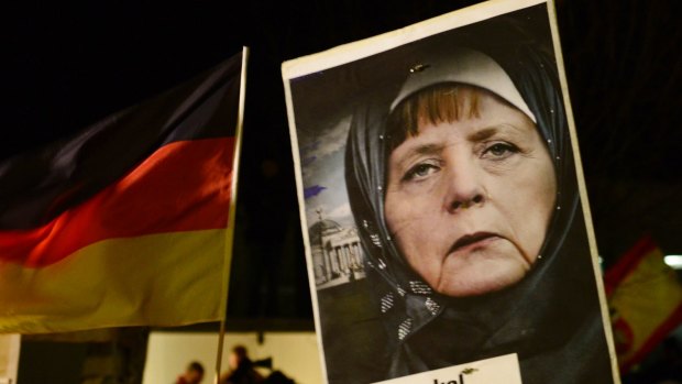 A protester in Dresden in 2015 holds a poster of German Chancellor Angela Merkel wearing an Islamic headscarf in front of a Reichstag building with a crescent on top.