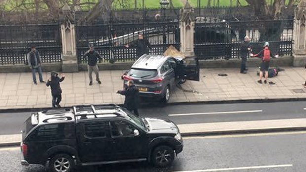 People stand near a crashed car and an injured person lying on the ground, right, on Bridge Street near the Houses of Parliament in London on Wednesday.