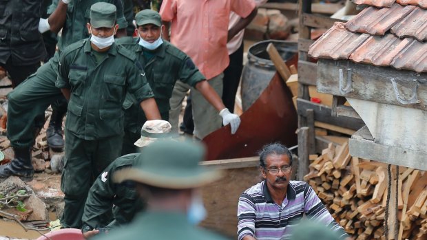 A Sri Lankan man helps military rescuers dig his buried house.