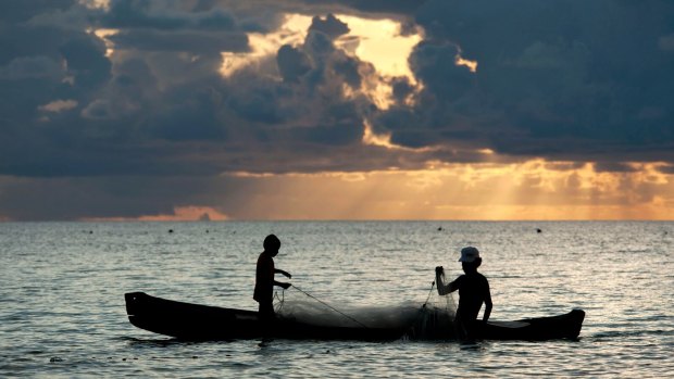 Father and son fishermen in dugout canoe bringing in a net at sunset, Ohoidertutu Village, Kei Islands, Moluccas, Indonesia. 