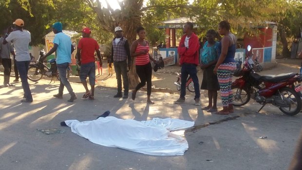 People stand by the body of a man who died when a bus crashed into a crowd watching street musicians in Haiti.