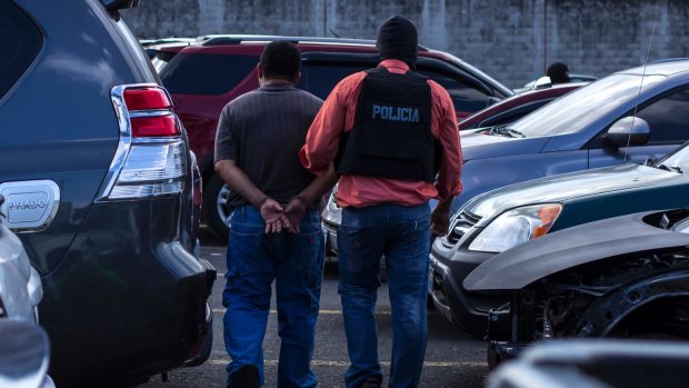 A suspected Mara Salvatrucha, or MS, gang member is taken away by a police officer after he was arrested and shown to the press in San Salvador.