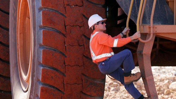 A worker climbs a ladder to enter the cab of a large ore moving truck at the Telfer Mine in the Pilbara region of Western Australia.