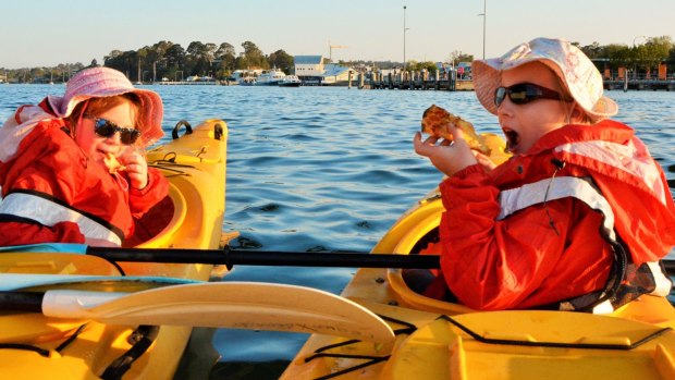 Emily and Sarah tuck into pizza in their kayaks under the Batemans Bay Bridge.