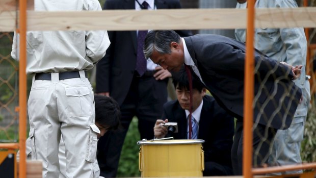Workers of Tokyo's Toshima ward office and police officers check a container holding a fragment of an unknown object after it was dug up from the ground near playground equipment at a park in Toshima ward, Tokyo.