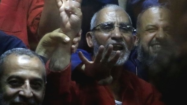 Egyptian defendants including the spiritual leader of the Muslim Brotherhood, Mohammed Badie, center, make a four-fingered gesture referring to the 2013 killing of Muslim Brotherhood protesters at the Rabaah Al-Adawiya mosque.