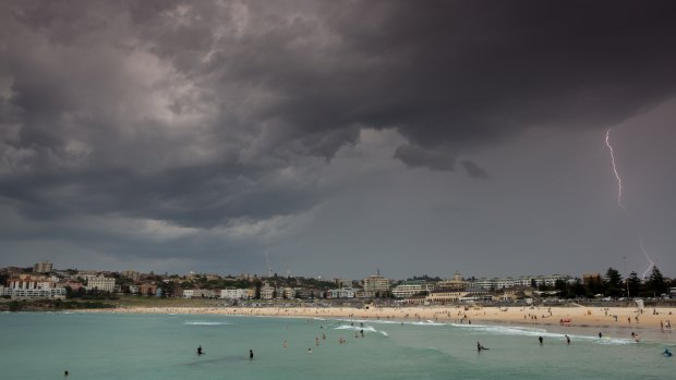 Swimmers at Bondi watch on as storm clouds gather and lightning flashes.