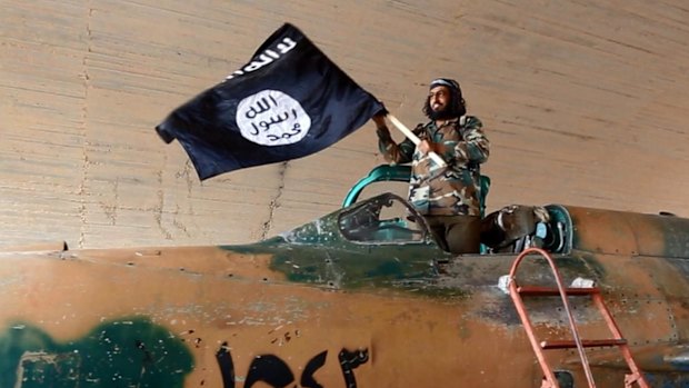 An Islamic State fighter waves a flag while standing on captured government fighter jet in Raqqa.