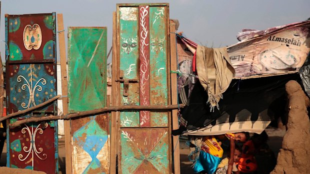 Children peek from their family's hut at a camp for internally displaced people near Abs, Yemen.