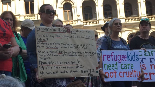 A woman holds up a sign with a message from a 21-year-old on Manus Island.