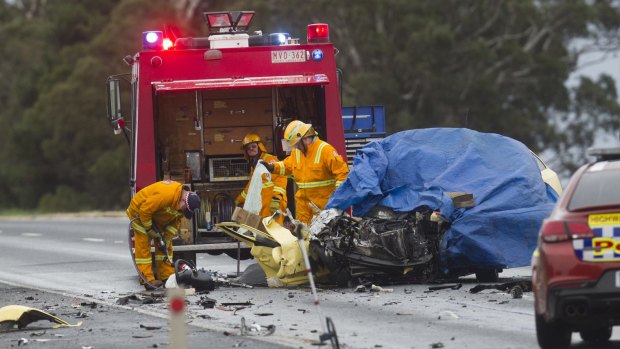 Emergency services examine the wreckage of a car that hit a truck in a head-on collision. 
